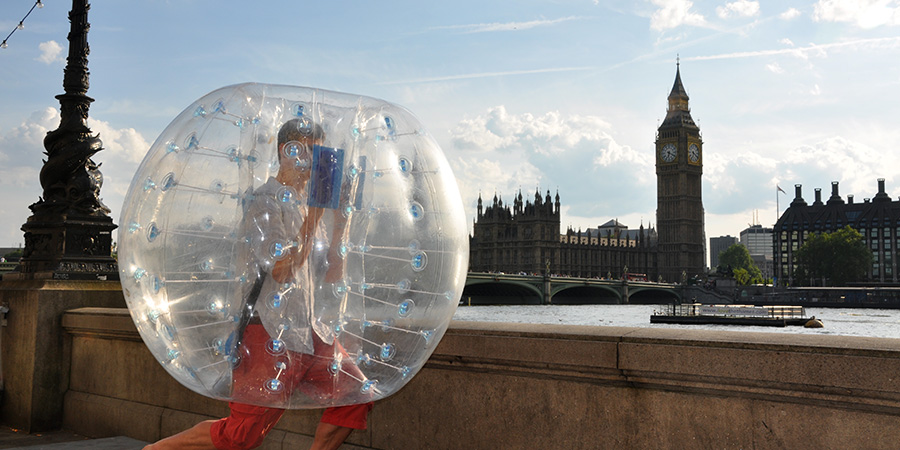 Man running inside a bubble football bubble along the Thames in front of Big Ben in Westminster