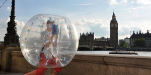 Man in bubble football body zorb running alongside Thames in London with Big Ben and Westminster in the background